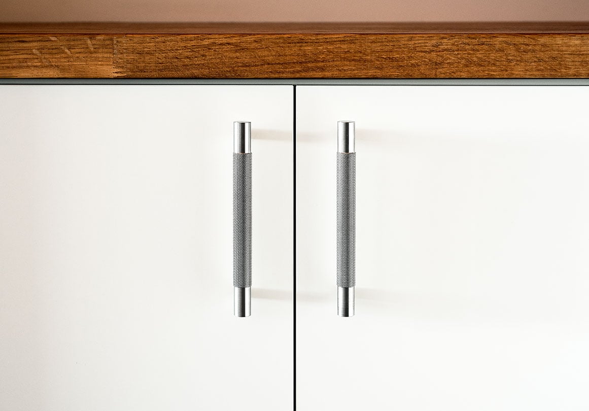 Kor Cabinet Pull in Stainless Steel with knurled texture installed on a white kitchen cabinet.
